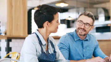 Two cafe workers sit in front of a laptop